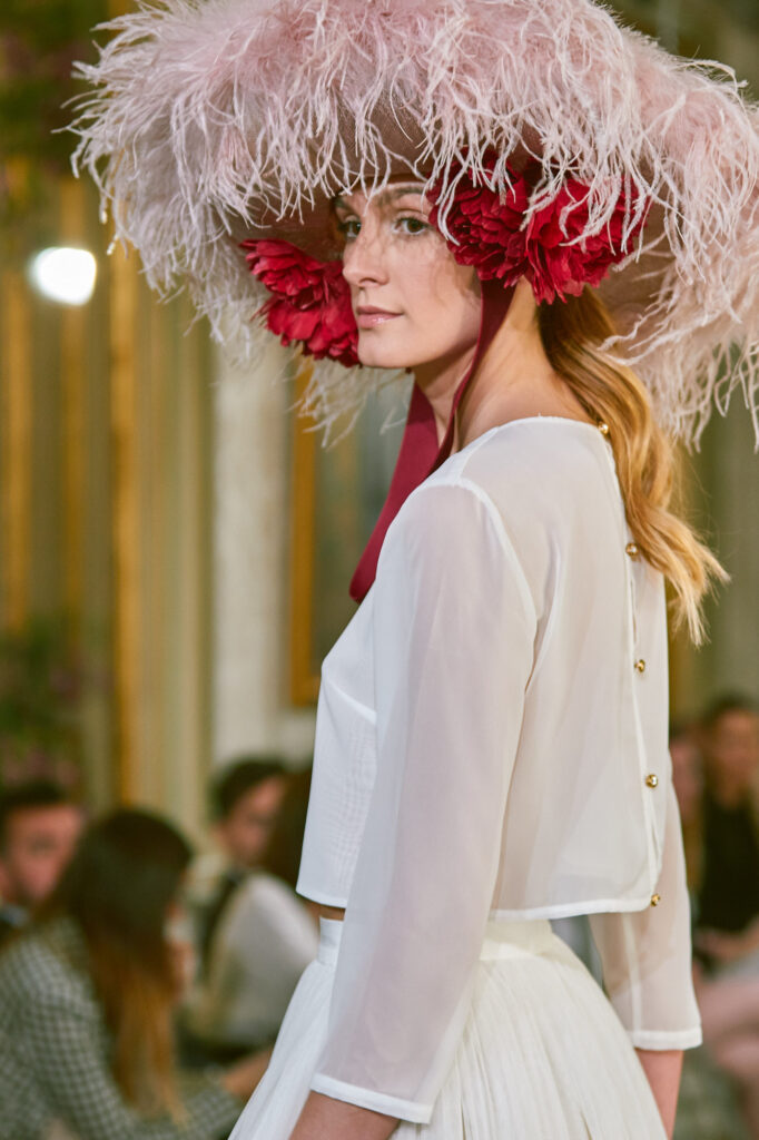 modelo en pasarella top blanco semitransparente con sombrero y detalle rojo